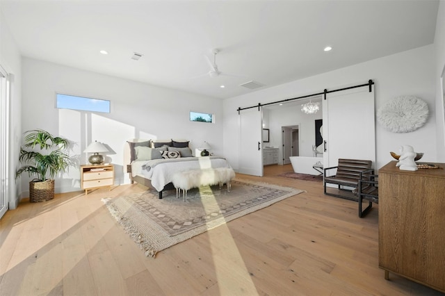 bedroom featuring a barn door, ceiling fan, and light wood-type flooring