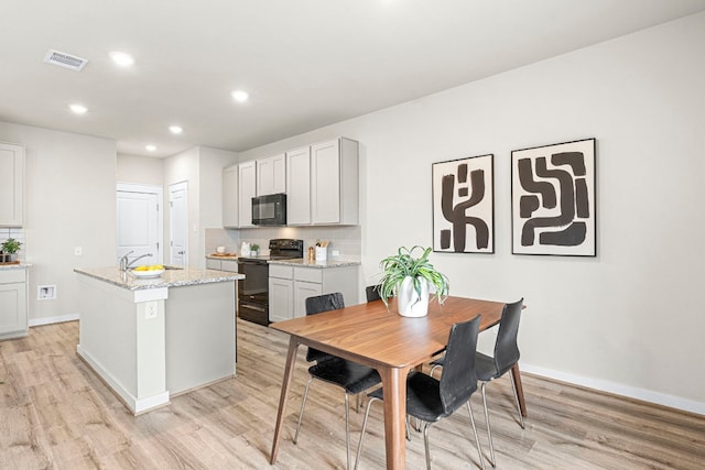 kitchen with light stone counters, light hardwood / wood-style floors, black appliances, an island with sink, and decorative backsplash