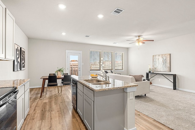 kitchen with sink, light stone counters, electric range oven, an island with sink, and light hardwood / wood-style floors