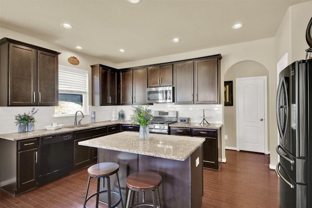 kitchen with light stone counters, dark brown cabinetry, stainless steel appliances, and a center island