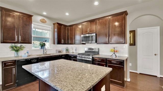 kitchen featuring dark brown cabinetry, sink, appliances with stainless steel finishes, a kitchen island, and light stone countertops