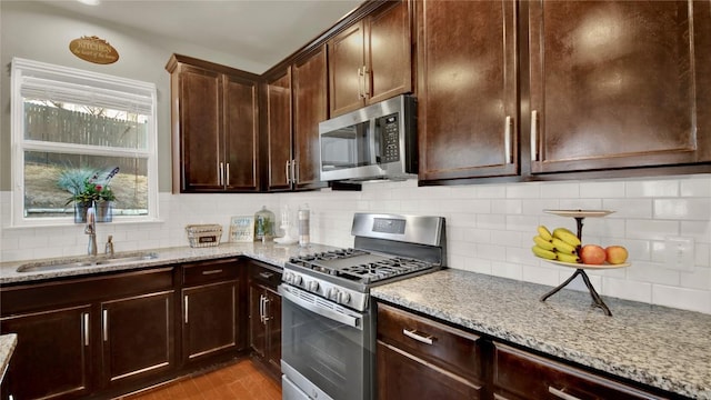 kitchen with tasteful backsplash, sink, light stone counters, stainless steel appliances, and light hardwood / wood-style flooring