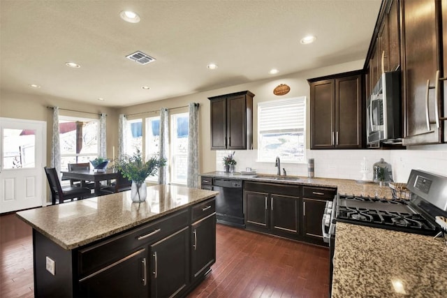 kitchen with sink, dark hardwood / wood-style flooring, a kitchen island, stainless steel appliances, and light stone countertops