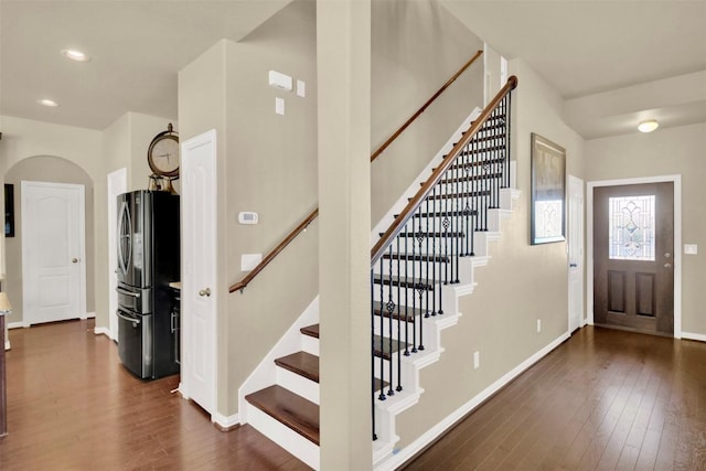 foyer with dark wood-style floors, recessed lighting, arched walkways, and baseboards