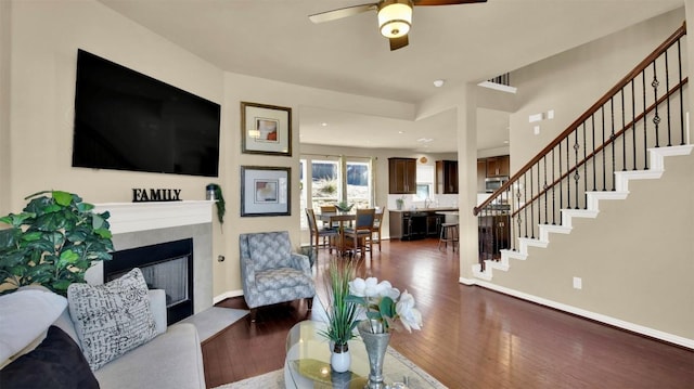 living area with wood-type flooring, stairway, a fireplace with raised hearth, and baseboards