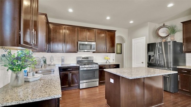 kitchen featuring backsplash, stainless steel appliances, a center island, light stone countertops, and dark hardwood / wood-style flooring