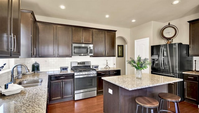 kitchen with sink, appliances with stainless steel finishes, a center island, light stone countertops, and dark hardwood / wood-style flooring