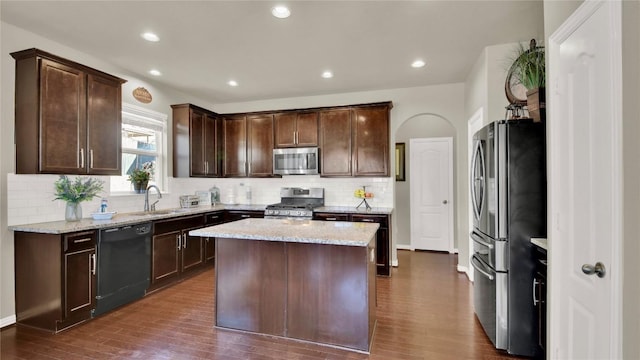 kitchen featuring sink, stainless steel appliances, dark brown cabinetry, light stone counters, and a kitchen island