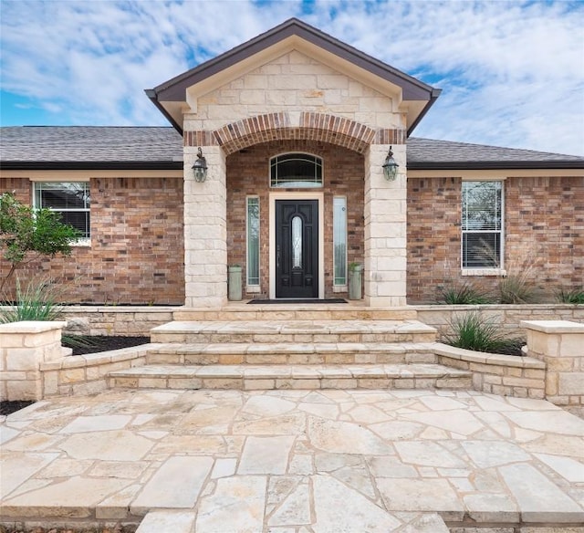 entrance to property with roof with shingles, stone siding, and brick siding