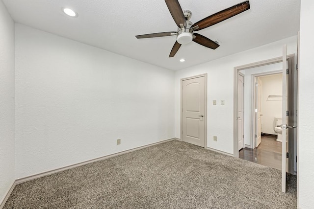 unfurnished bedroom with ensuite bath, ceiling fan, and dark colored carpet