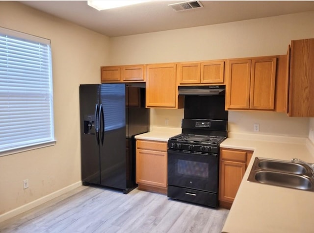 kitchen featuring sink, extractor fan, light wood-type flooring, a wealth of natural light, and black appliances