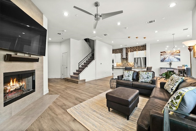 living room featuring a tiled fireplace, ceiling fan with notable chandelier, and light hardwood / wood-style floors