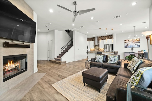 living room with stairway, a tile fireplace, light wood finished floors, visible vents, and recessed lighting