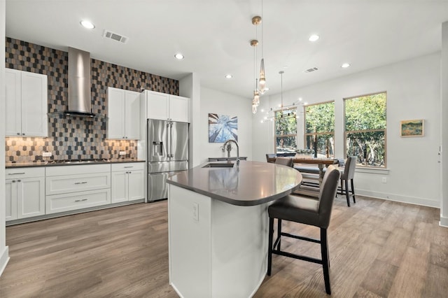 kitchen with stainless steel appliances, dark countertops, visible vents, wall chimney range hood, and a sink