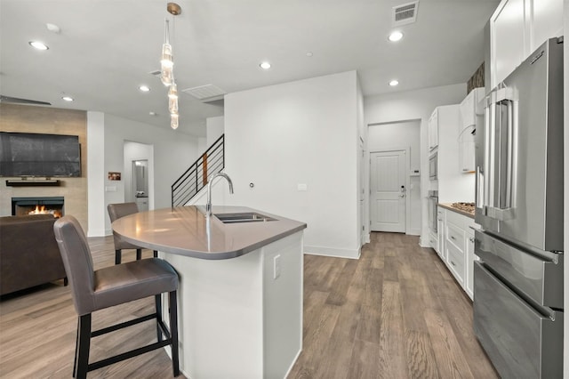 kitchen with a sink, light wood-style floors, a large fireplace, an island with sink, and appliances with stainless steel finishes