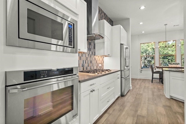 kitchen with recessed lighting, wall chimney exhaust hood, tasteful backsplash, appliances with stainless steel finishes, and white cabinetry