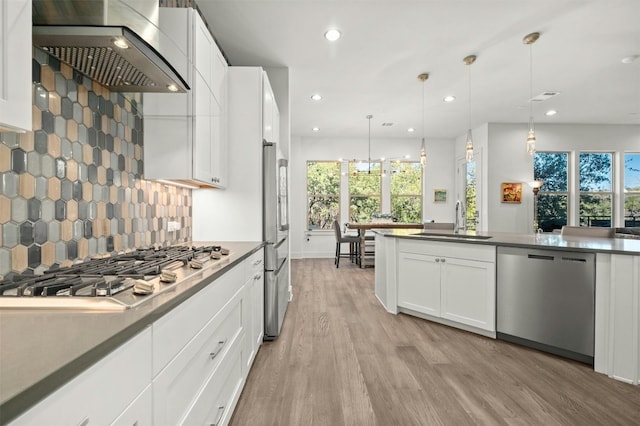 kitchen featuring wall chimney range hood, a sink, plenty of natural light, light wood-type flooring, and stainless steel appliances