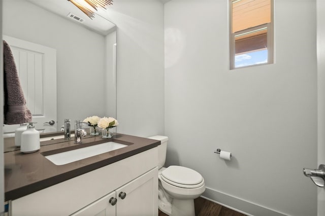 half bath with wood finished floors, visible vents, toilet, vanity, and baseboards