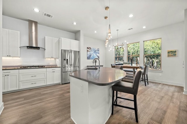 kitchen with stainless steel appliances, dark countertops, wall chimney range hood, visible vents, and a sink