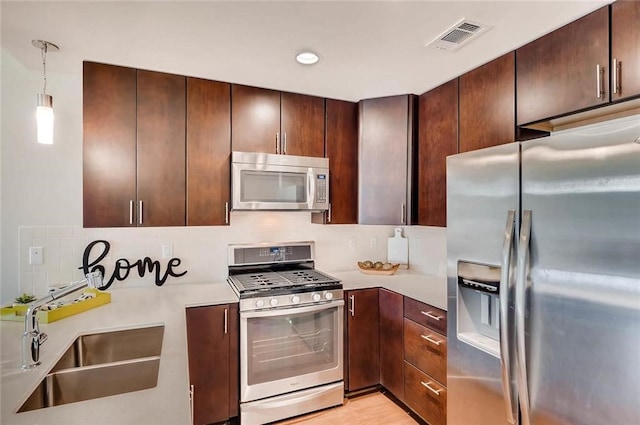 kitchen with dark brown cabinetry, sink, hanging light fixtures, appliances with stainless steel finishes, and decorative backsplash