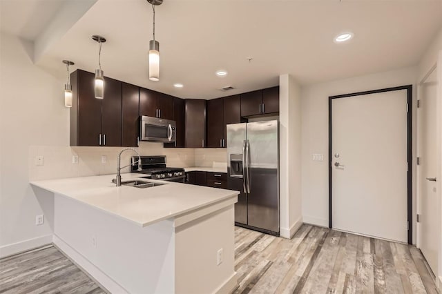 kitchen featuring decorative backsplash, dark brown cabinetry, stainless steel appliances, light countertops, and a peninsula