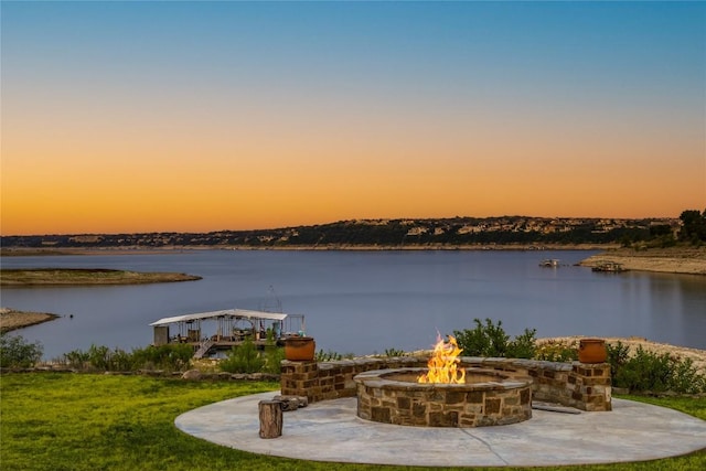 patio terrace at dusk featuring a yard, a fire pit, and a water view