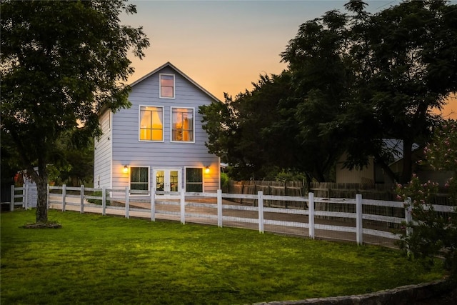 property exterior at dusk featuring a lawn and french doors