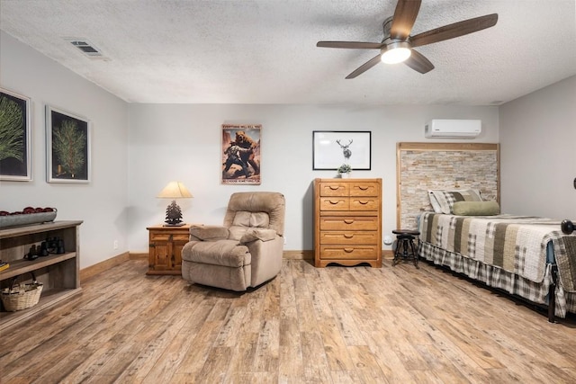 bedroom featuring visible vents, baseboards, an AC wall unit, light wood-style floors, and a textured ceiling