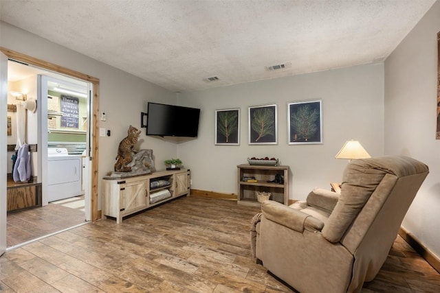 living room featuring washer / dryer, wood finished floors, visible vents, and a textured ceiling