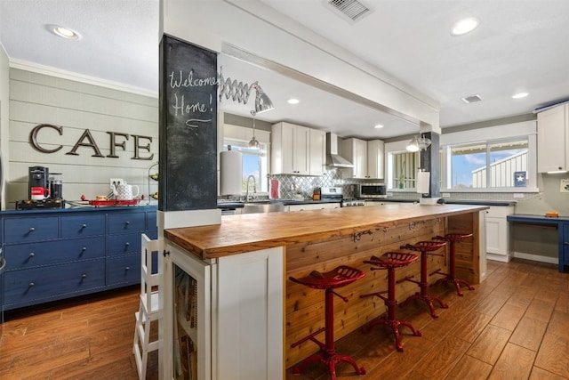 kitchen with visible vents, dark wood-type flooring, wall chimney range hood, stainless steel range, and wood counters