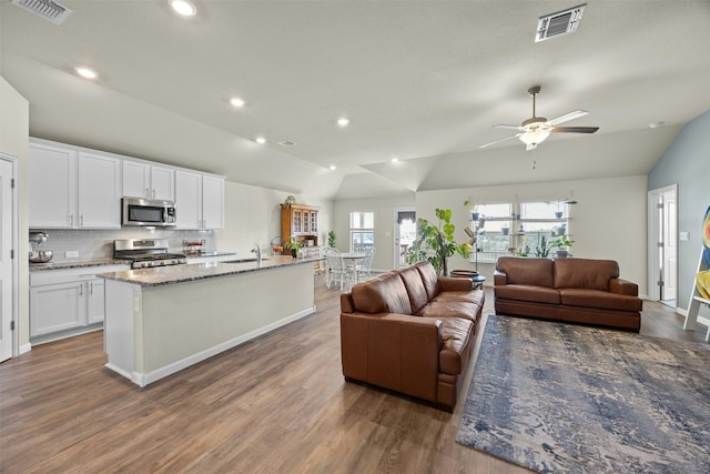 kitchen with white cabinetry, light stone counters, vaulted ceiling, a center island with sink, and appliances with stainless steel finishes