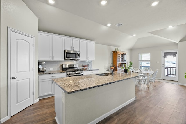 kitchen with light stone counters, stainless steel appliances, an island with sink, and white cabinets