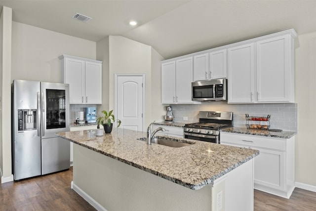 kitchen with sink, appliances with stainless steel finishes, white cabinetry, light stone counters, and a center island with sink