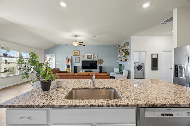 kitchen featuring sink, a kitchen island with sink, stainless steel appliances, light stone countertops, and washer / clothes dryer