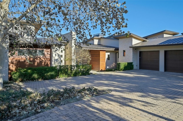 contemporary house featuring decorative driveway, a garage, stone siding, and a chimney