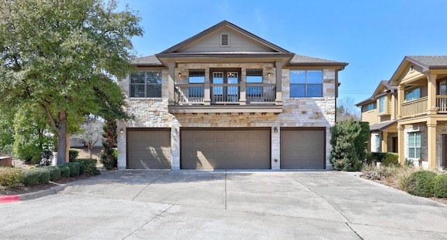 view of front of home with stone siding, an attached garage, a balcony, and driveway