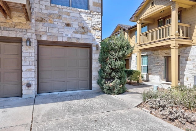 exterior space featuring a garage, stone siding, and a balcony