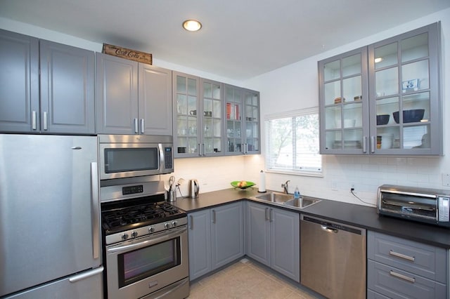 kitchen with appliances with stainless steel finishes, a sink, gray cabinets, dark countertops, and tasteful backsplash