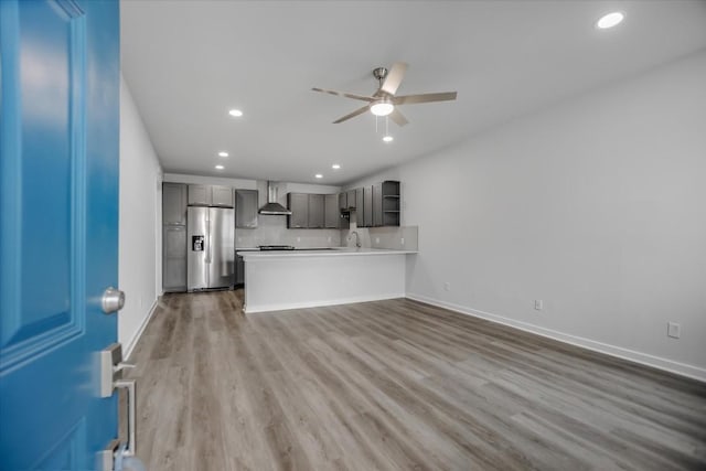 kitchen featuring stainless steel refrigerator with ice dispenser, gray cabinets, hardwood / wood-style flooring, ceiling fan, and wall chimney range hood