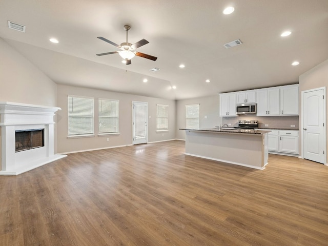 kitchen with appliances with stainless steel finishes, an island with sink, white cabinets, ceiling fan, and light hardwood / wood-style floors