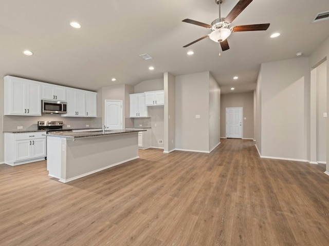 kitchen with an island with sink, appliances with stainless steel finishes, white cabinets, and light hardwood / wood-style floors