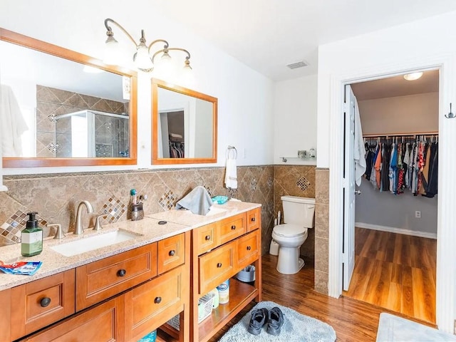 bathroom featuring a shower with shower door, wood-type flooring, tile walls, vanity, and toilet