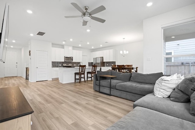 living room featuring ceiling fan with notable chandelier and light hardwood / wood-style flooring