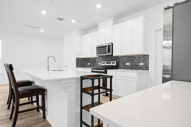 kitchen with appliances with stainless steel finishes, a breakfast bar, white cabinetry, sink, and a center island with sink