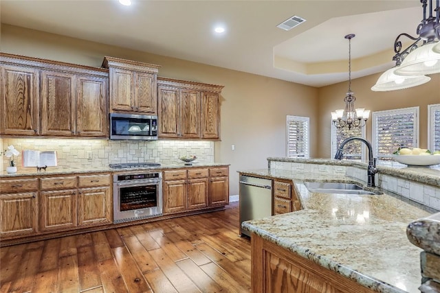 kitchen with appliances with stainless steel finishes, pendant lighting, sink, decorative backsplash, and a tray ceiling