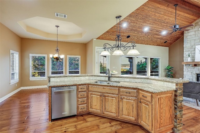 kitchen featuring dishwasher, an island with sink, sink, a tray ceiling, and light wood-type flooring