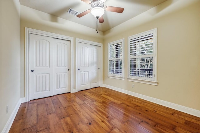 unfurnished bedroom featuring multiple closets, ceiling fan, and hardwood / wood-style flooring