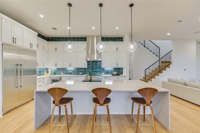 kitchen with white cabinetry, a kitchen bar, hanging light fixtures, stainless steel built in fridge, and wall chimney exhaust hood