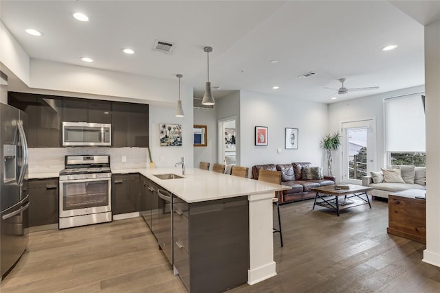 kitchen with a breakfast bar, sink, decorative light fixtures, appliances with stainless steel finishes, and kitchen peninsula