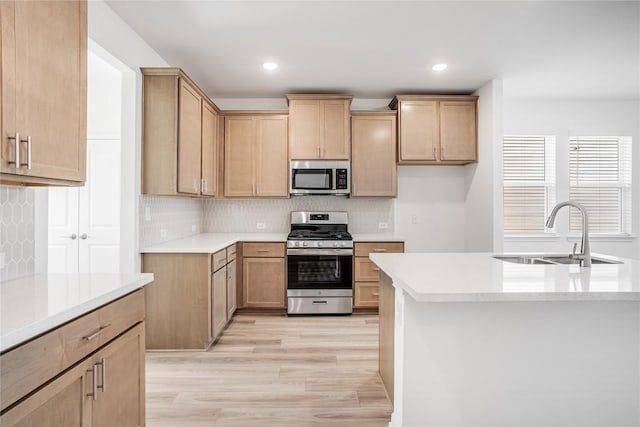 kitchen featuring tasteful backsplash, light countertops, light wood-style flooring, appliances with stainless steel finishes, and a sink